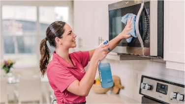 Molly Maid cleaner wiping down microwave.